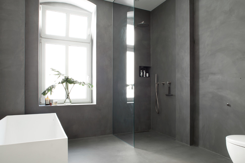 Photo of a large contemporary master bathroom in Berlin with furniture-like cabinets, grey cabinets, a freestanding tub, an open shower, a one-piece toilet, grey walls, concrete floors, a pedestal sink and granite benchtops.