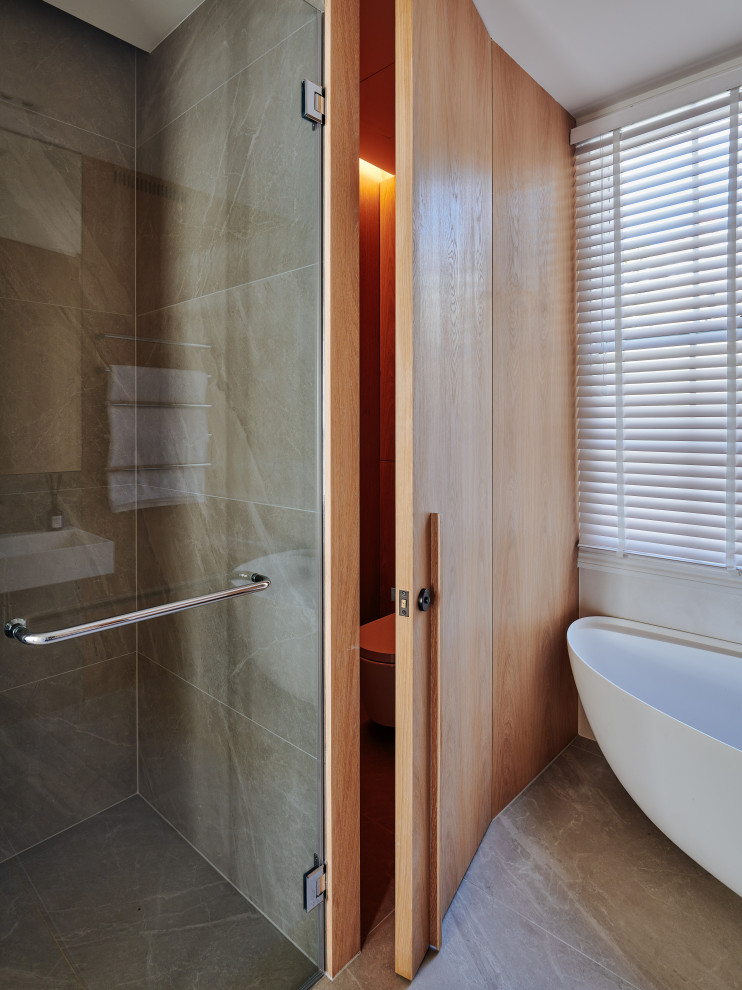 Inredning av ett 60 tals stort en-suite badrum, med ett fristående badkar, en öppen dusch, en vägghängd toalettstol, grå kakel, kakelplattor, grå väggar, kalkstensgolv, grått golv och dusch med gångjärnsdörr
