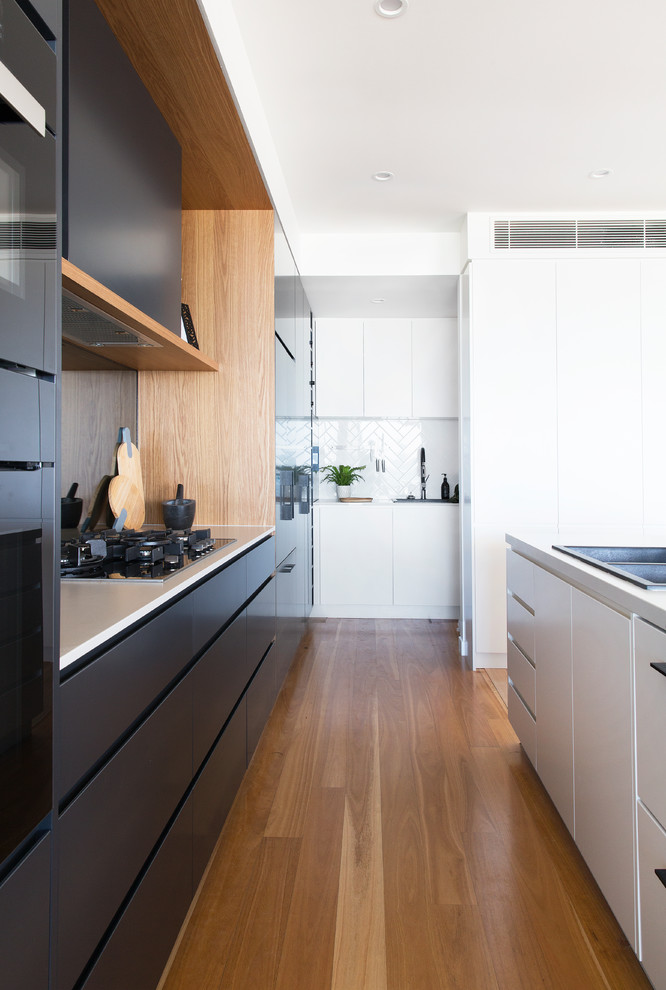 Design ideas for a large contemporary galley kitchen pantry in Gold Coast - Tweed with a drop-in sink, flat-panel cabinets, black cabinets, quartz benchtops, mirror splashback, black appliances, light hardwood floors, with island and beige floor.