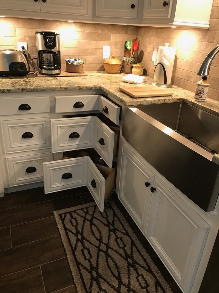 Inspiration for a large transitional l-shaped brown floor eat-in kitchen remodel in Birmingham with a farmhouse sink, recessed-panel cabinets, white cabinets, beige backsplash, stainless steel appliances and an island