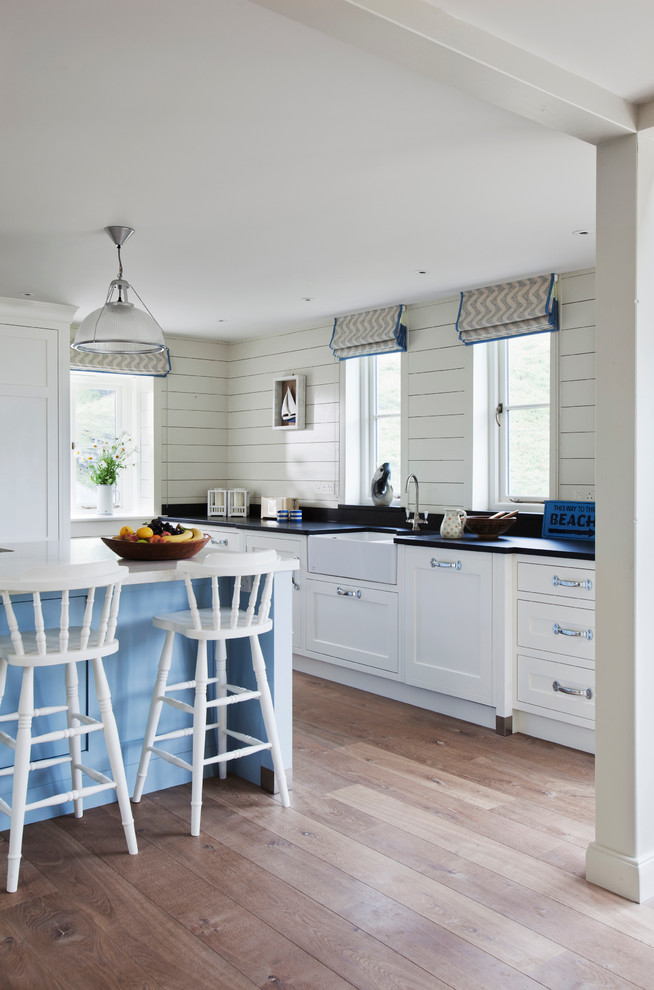Design ideas for a beach style kitchen in Wiltshire with a farmhouse sink, recessed-panel cabinets, white cabinets, panelled appliances, quartz benchtops, medium hardwood floors and with island.