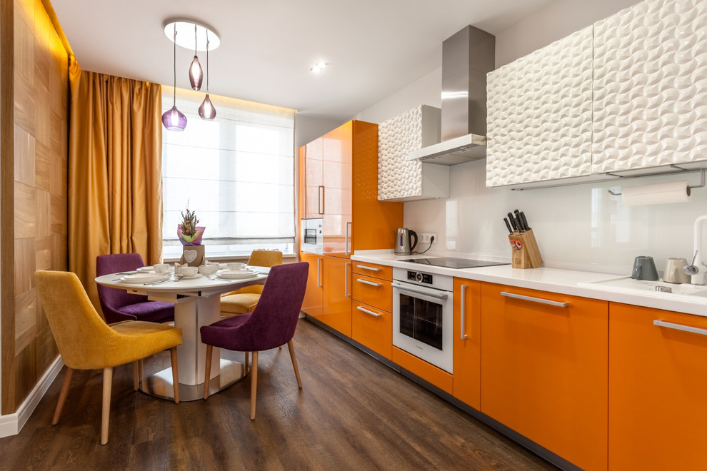 This is an example of a mid-sized eclectic single-wall open plan kitchen in Yekaterinburg with an undermount sink, white splashback, glass sheet splashback, white appliances, vinyl floors, brown floor, flat-panel cabinets, orange cabinets, solid surface benchtops, no island and white benchtop.