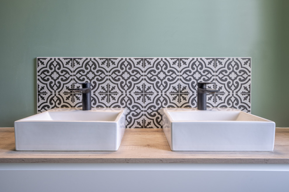 This is an example of a mid-sized mediterranean master bathroom in Rennes with beaded inset cabinets, white cabinets, a curbless shower, black and white tile, cement tile, green walls, vinyl floors, a drop-in sink, wood benchtops, brown floor, an open shower, brown benchtops, a double vanity and a floating vanity.
