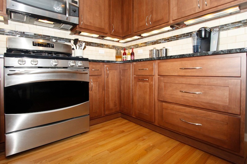 Inspiration for a mid-sized transitional u-shaped light wood floor enclosed kitchen remodel in Chicago with an undermount sink, shaker cabinets, medium tone wood cabinets, granite countertops, beige backsplash, stone tile backsplash, stainless steel appliances and no island