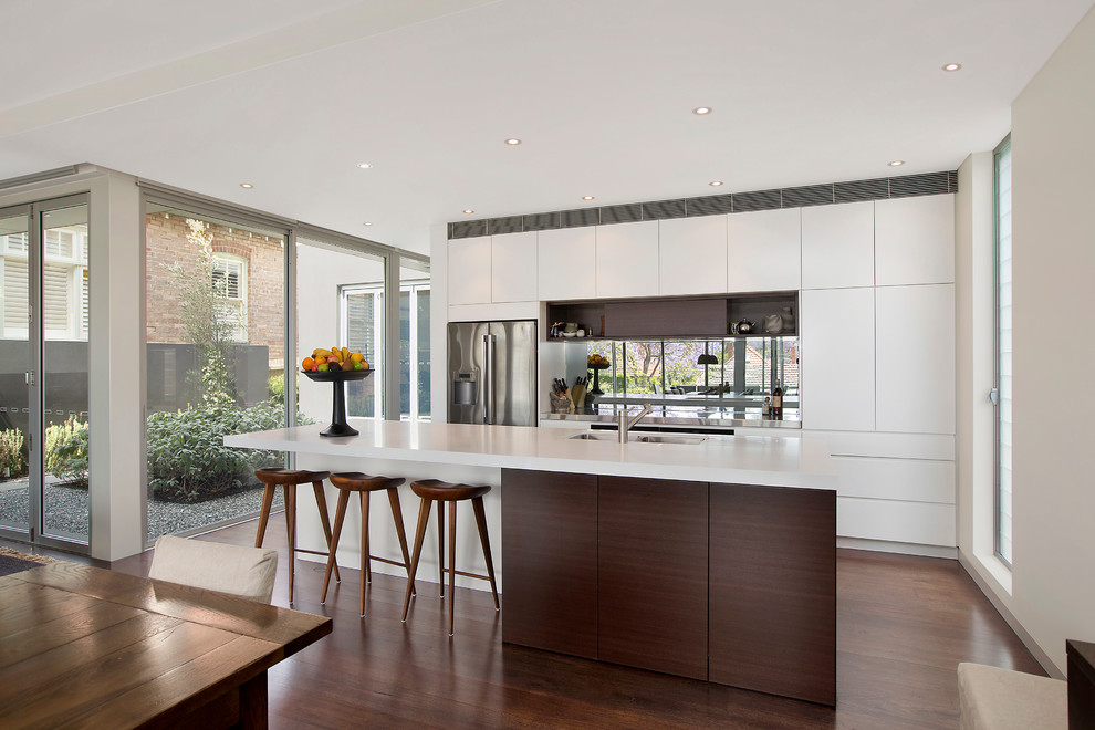 Photo of a contemporary kitchen in Sydney with a double-bowl sink, white cabinets, glass sheet splashback, stainless steel appliances, dark hardwood floors and with island.