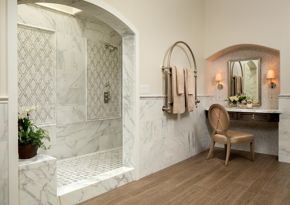 This is an example of a large traditional master bathroom in Orange County with recessed-panel cabinets, grey cabinets, an open shower, stone tile, porcelain floors, marble benchtops, beige walls, brown floor and an open shower.
