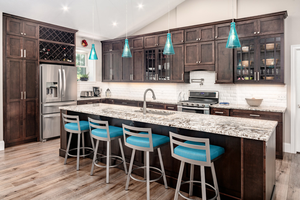 Design ideas for a transitional l-shaped kitchen in Other with an undermount sink, shaker cabinets, dark wood cabinets, white splashback, subway tile splashback, stainless steel appliances, medium hardwood floors, with island and brown floor.