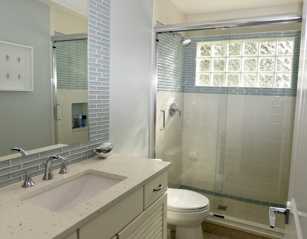 Mid-sized beach style 3/4 bathroom in Jacksonville with louvered cabinets, white cabinets, an alcove shower, a two-piece toilet, blue tile, white tile, subway tile, white walls, an undermount sink, beige floor and a sliding shower screen.