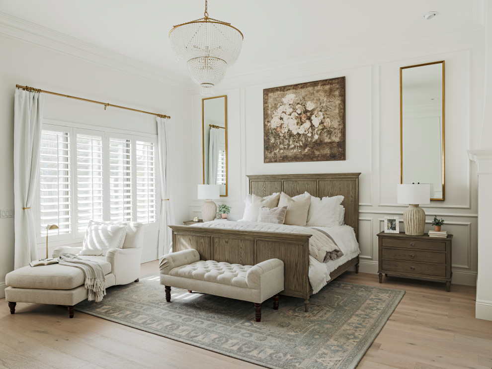 Imagen de dormitorio principal grande con paredes blancas, suelo de madera clara, chimenea de esquina, marco de chimenea de yeso, suelo beige, todos los diseños de techos y panelado