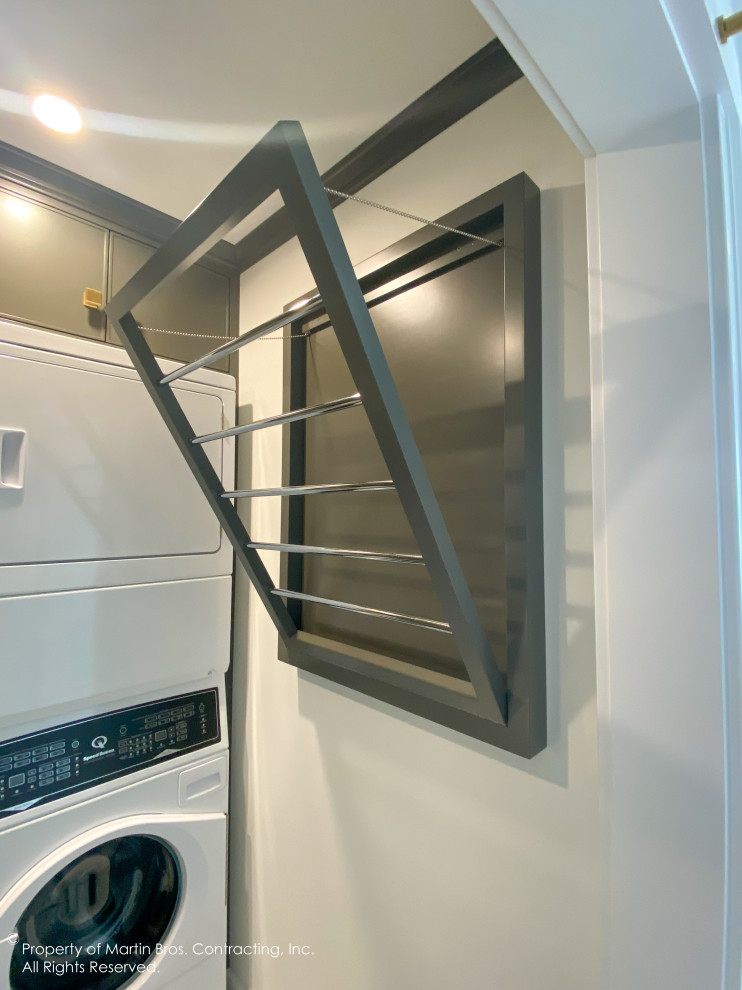 Example of a mid-sized transitional l-shaped porcelain tile and white floor dedicated laundry room design with an undermount sink, flat-panel cabinets, gray cabinets, quartzite countertops, stone slab backsplash, white walls and a stacked washer/dryer