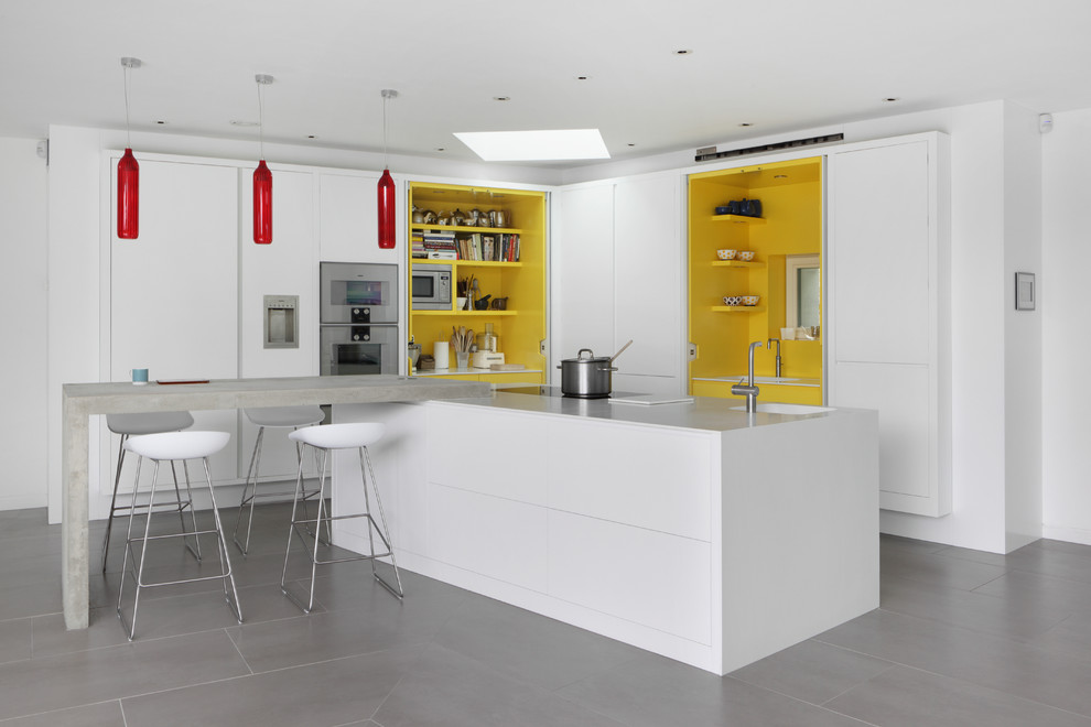 Photo of a mid-sized contemporary l-shaped eat-in kitchen in London with a drop-in sink, flat-panel cabinets, white cabinets, laminate benchtops, yellow splashback, stainless steel appliances, porcelain floors and multiple islands.