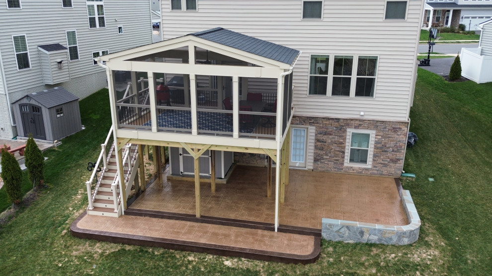 Cette image montre un très grand porche d'entrée de maison arrière traditionnel avec une moustiquaire, du béton estampé, une extension de toiture et un garde-corps en matériaux mixtes.