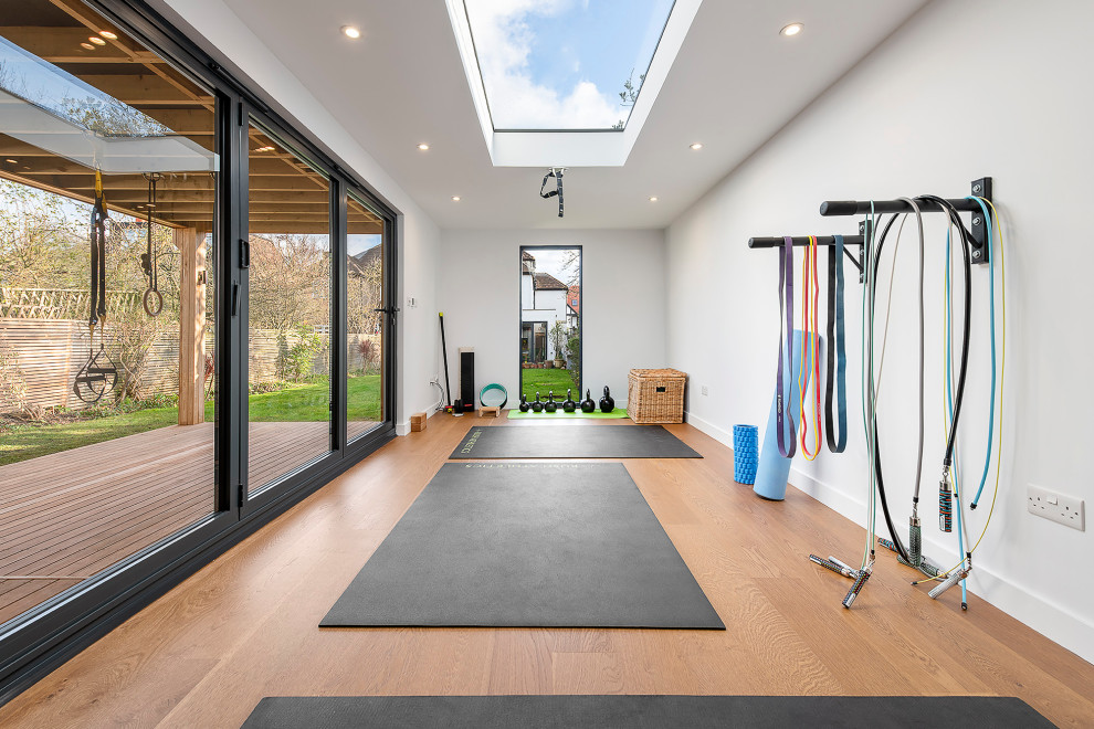 Multifunktionaler, Großer Moderner Fitnessraum mit weißer Wandfarbe, hellem Holzboden und schwarzem Boden in London