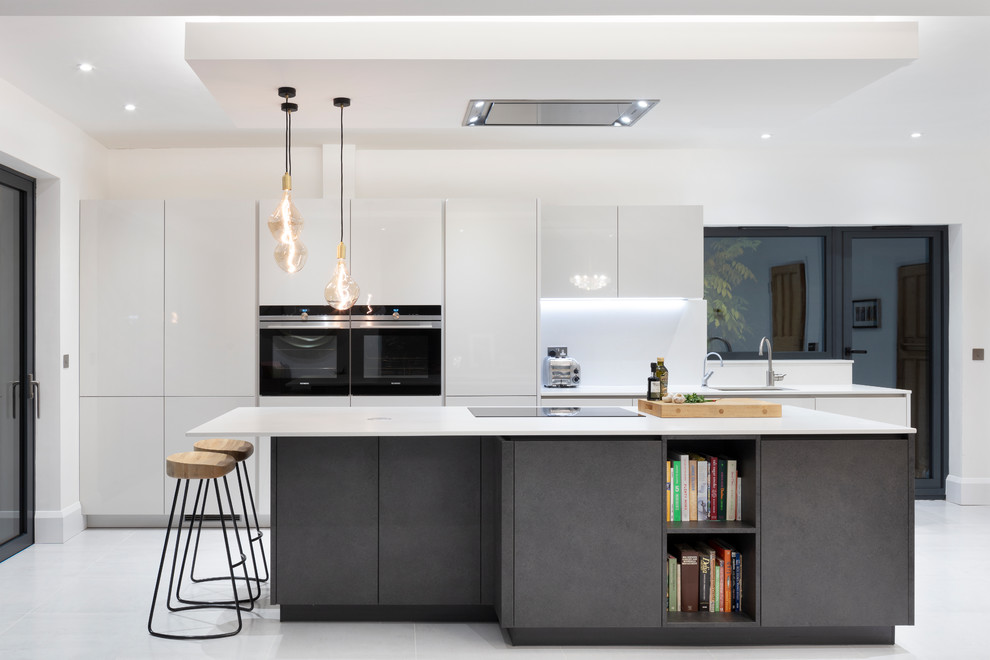 This is an example of a mid-sized contemporary galley open plan kitchen in London with flat-panel cabinets, grey cabinets, quartzite benchtops, grey splashback, stone slab splashback, black appliances, porcelain floors, with island, grey floor, an undermount sink and white benchtop.