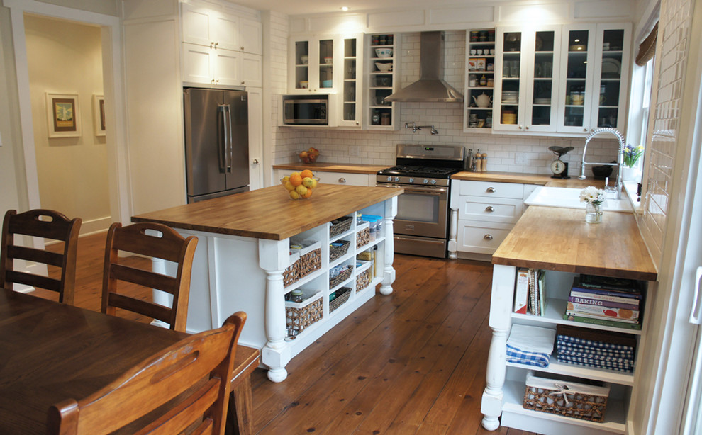 Example of a large transitional u-shaped medium tone wood floor open concept kitchen design in Ottawa with a farmhouse sink, shaker cabinets, distressed cabinets, wood countertops, white backsplash, subway tile backsplash, stainless steel appliances and an island