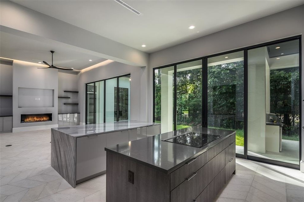 Contemporary l-shaped open plan kitchen in Houston with flat-panel cabinets, grey cabinets, marble benchtops, grey splashback, marble splashback, stainless steel appliances, travertine floors, multiple islands, grey benchtop and grey floor.