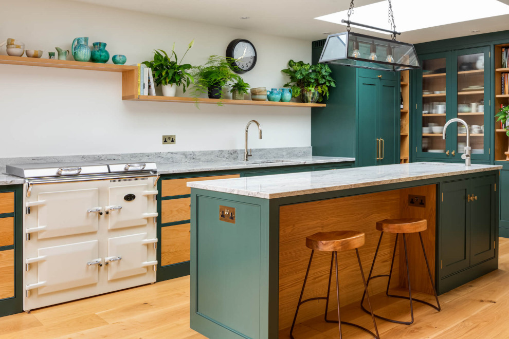 Photo of a large classic l-shaped open plan kitchen in Gloucestershire with a submerged sink, shaker cabinets, green cabinets, granite worktops, stainless steel appliances, an island, grey worktops and a feature wall.