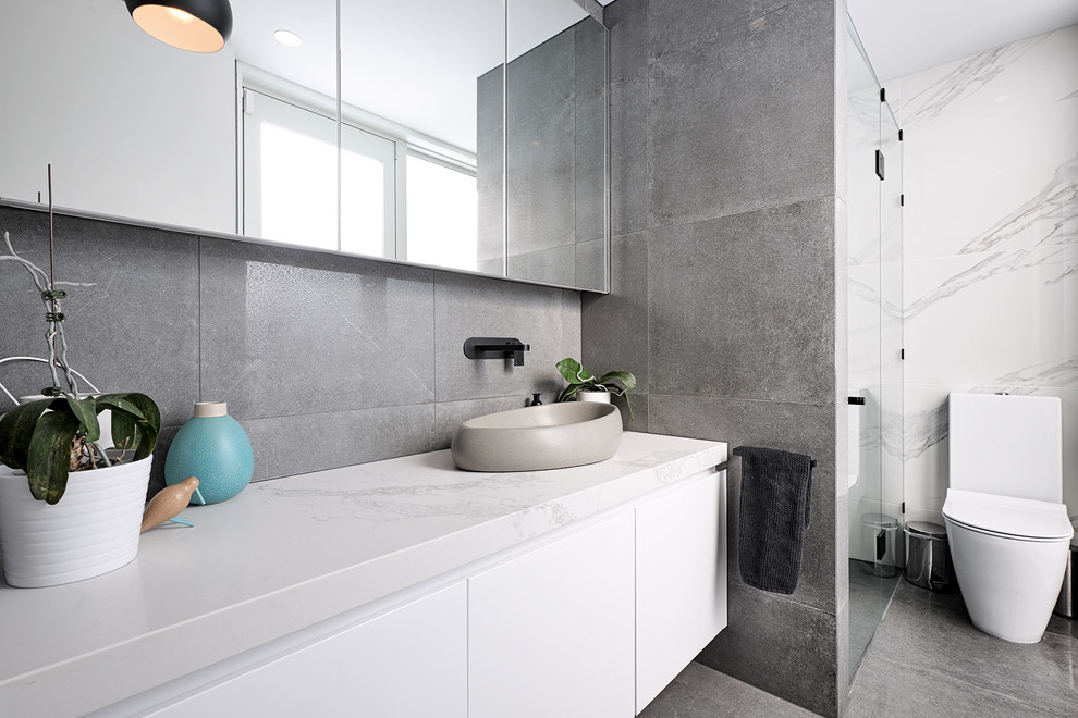 Inspiration for a mid-sized modern master bathroom in Melbourne with shaker cabinets, white cabinets, a drop-in tub, a shower/bathtub combo, a two-piece toilet, gray tile, ceramic tile, grey walls, cement tiles, a vessel sink, granite benchtops, grey floor, a hinged shower door and white benchtops.