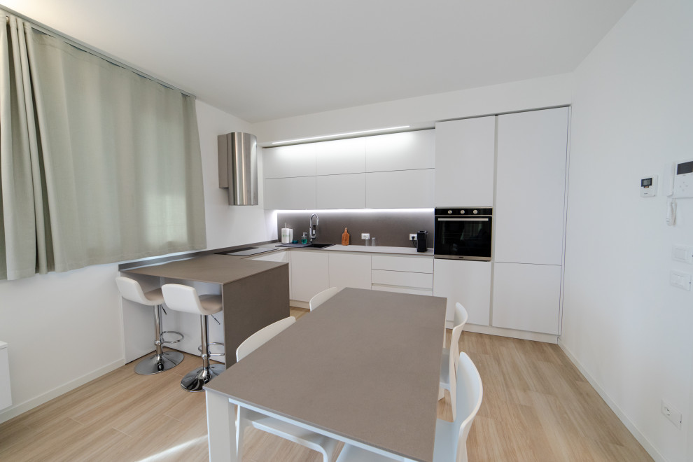 Design ideas for a large modern l-shaped eat-in kitchen in Milan with a drop-in sink, flat-panel cabinets, white cabinets, quartz benchtops, brown splashback, engineered quartz splashback, black appliances, porcelain floors, a peninsula, beige floor and brown benchtop.