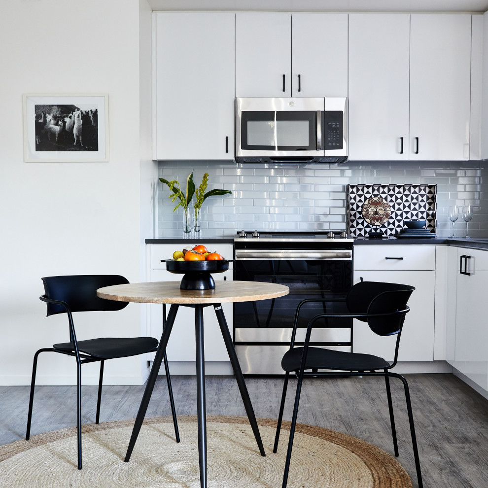 Photo of a small modern l-shaped eat-in kitchen in San Francisco with flat-panel cabinets, white cabinets, quartz benchtops, blue splashback, ceramic splashback, stainless steel appliances, vinyl floors, no island, grey floor and black benchtop.