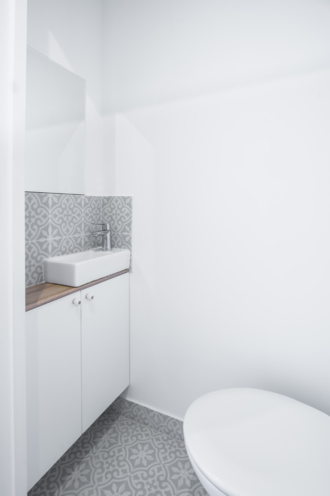 Small transitional powder room in Paris with flat-panel cabinets, white cabinets, a wall-mount toilet, white walls, ceramic floors, a console sink, wood benchtops, multi-coloured floor and beige benchtops.