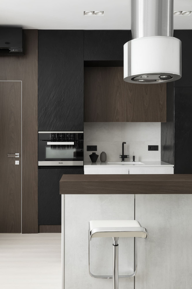 This is an example of a mid-sized contemporary single-wall open plan kitchen in Moscow with an undermount sink, flat-panel cabinets, black cabinets, quartz benchtops, grey splashback, porcelain splashback, black appliances, light hardwood floors, with island, beige floor and white benchtop.