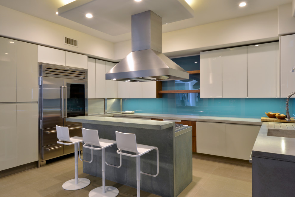 This is an example of a mid-sized contemporary l-shaped eat-in kitchen in San Diego with flat-panel cabinets, white cabinets, concrete benchtops, blue splashback, stainless steel appliances, with island, an integrated sink and glass sheet splashback.