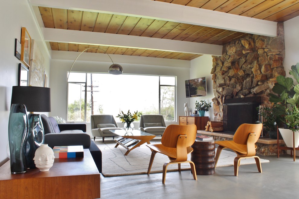 Photo of a midcentury living room in Los Angeles with white walls, concrete floors, a standard fireplace, a stone fireplace surround and a wall-mounted tv.