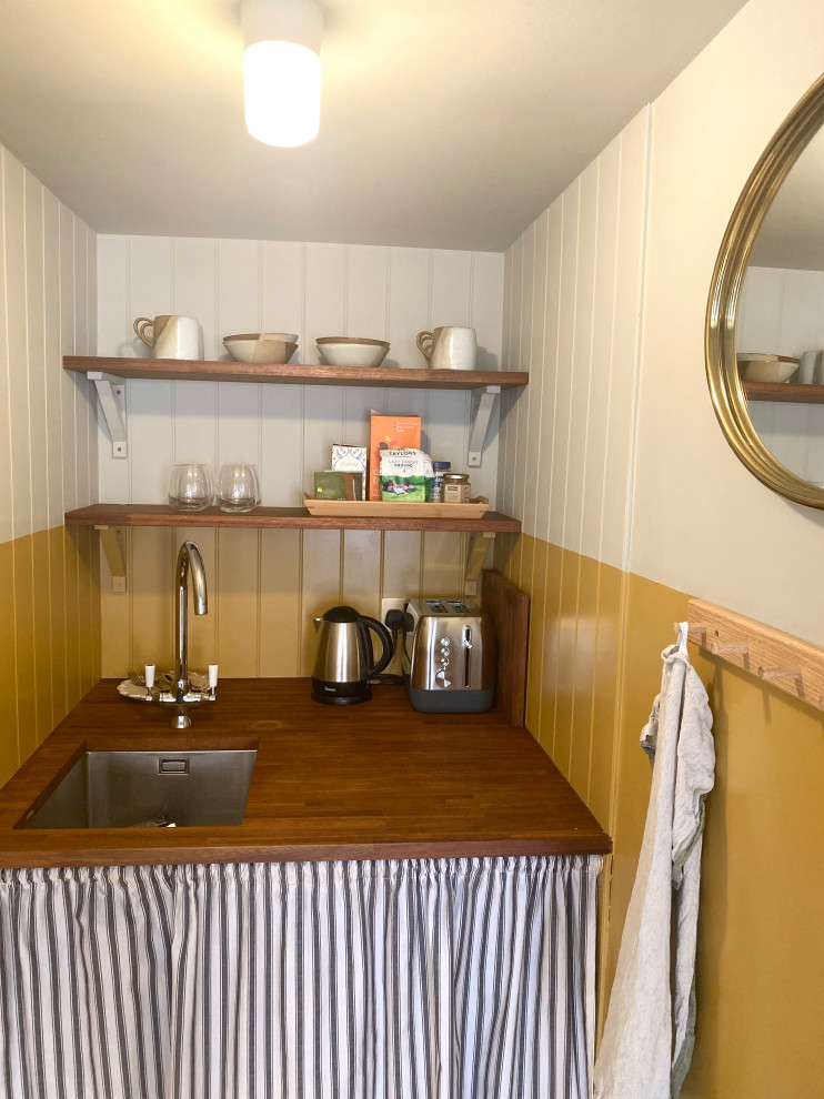 This is an example of a small beach style single-wall kitchen pantry in Kent with a drop-in sink, open cabinets, dark wood cabinets, wood benchtops, yellow splashback, shiplap splashback, stainless steel appliances, vinyl floors, no island, beige floor and brown benchtop.
