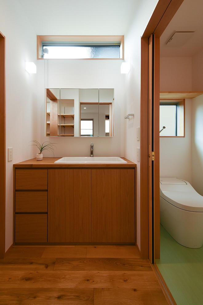 Design ideas for a mid-sized asian powder room in Other with a one-piece toilet, white tile, white walls, wood benchtops, brown benchtops, flat-panel cabinets, dark wood cabinets, medium hardwood floors, an undermount sink, beige floor, a built-in vanity, wallpaper and wallpaper.
