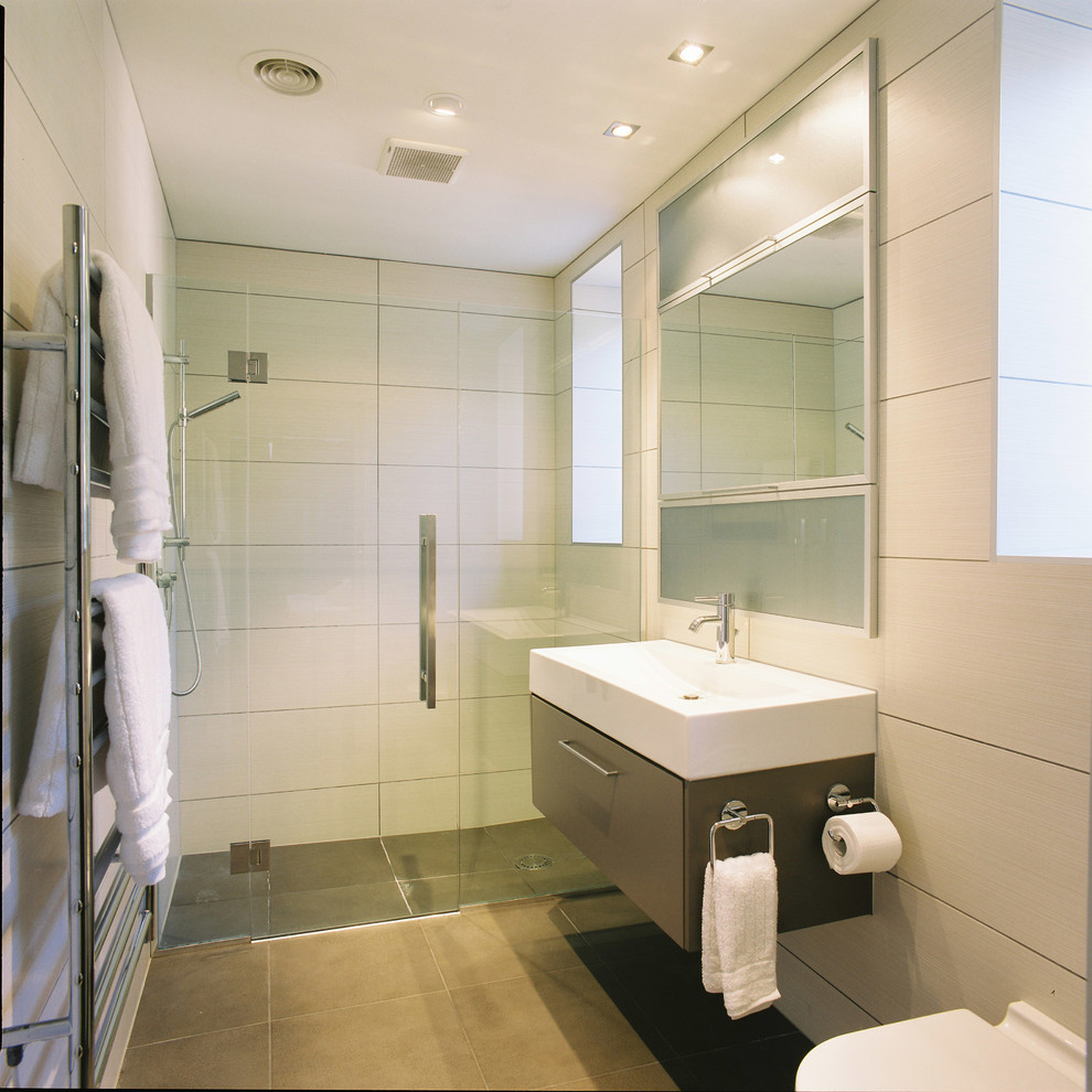 This is an example of a contemporary bathroom in Other with a wall-mount sink, flat-panel cabinets, a curbless shower and beige tile.