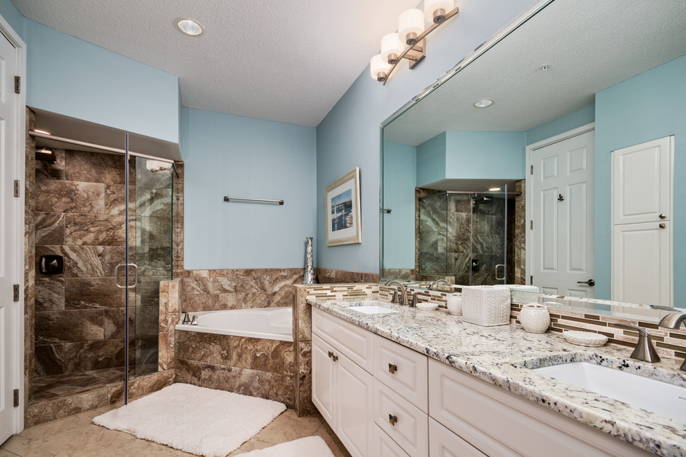 Photo of a mid-sized beach style bathroom in Miami with an undermount sink, raised-panel cabinets, white cabinets, granite benchtops, a corner tub, a corner shower, beige tile, ceramic tile, blue walls and travertine floors.