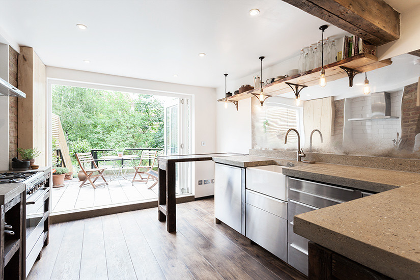 Photo of a mid-sized scandinavian galley separate kitchen in London with a farmhouse sink, flat-panel cabinets, stainless steel cabinets, concrete benchtops, mirror splashback, stainless steel appliances, dark hardwood floors and a peninsula.