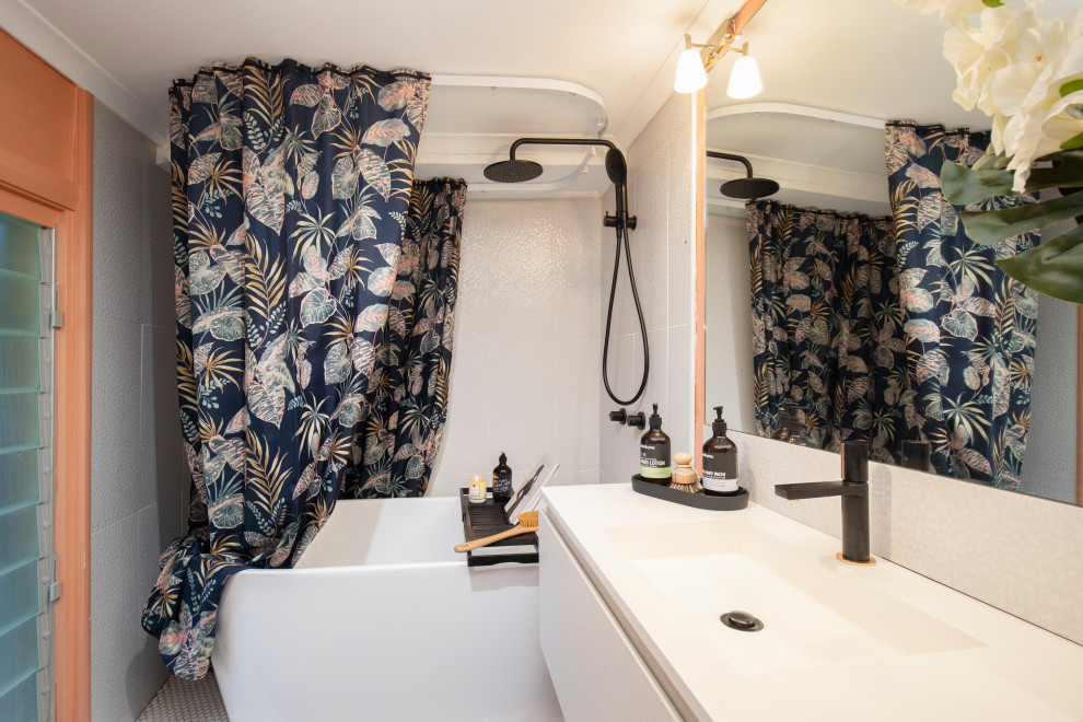 Стильный дизайн: главная ванная комната среднего размера со стиральной машиной в средиземноморском стиле с бежевыми фасадами, отдельно стоящей ванной, душем над ванной, унитазом-моноблоком, белой плиткой, керамической плиткой, оранжевыми стенами, полом из керамической плитки, монолитной раковиной, столешницей из искусственного кварца, серым полом, шторкой для ванной, белой столешницей, тумбой под одну раковину и подвесной тумбой - последний тренд
