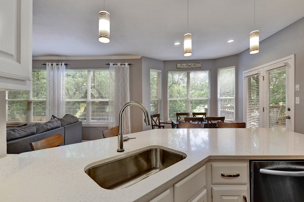 Example of a mid-sized transitional u-shaped light wood floor eat-in kitchen design in Austin with an undermount sink, white cabinets, quartz countertops, white backsplash, stone slab backsplash, stainless steel appliances, a peninsula and raised-panel cabinets