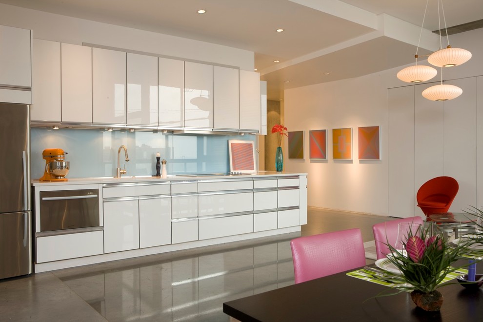 This is an example of a modern single-wall kitchen in Kansas City with stainless steel appliances, flat-panel cabinets, white cabinets, blue splashback and glass sheet splashback.