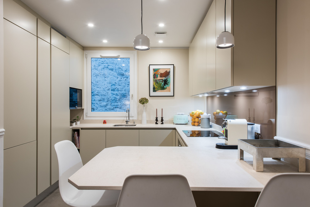 This is an example of a contemporary u-shaped kitchen in Paris with an undermount sink, flat-panel cabinets, beige cabinets, brown splashback, glass sheet splashback and a peninsula.