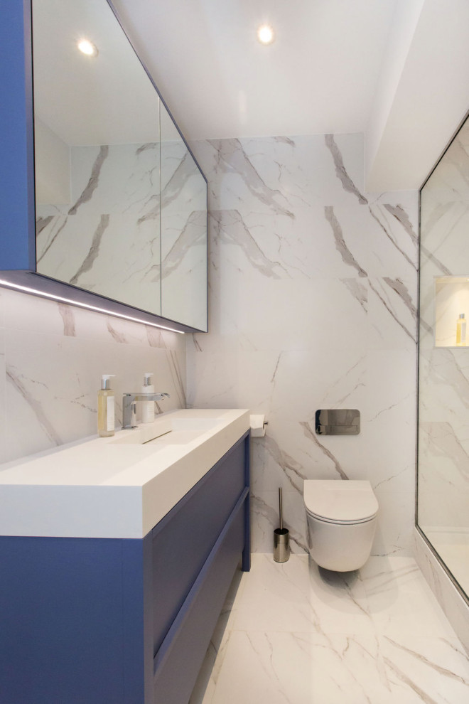 This is an example of a mid-sized contemporary master bathroom in London with recessed-panel cabinets, blue cabinets, white tile, marble and marble benchtops.