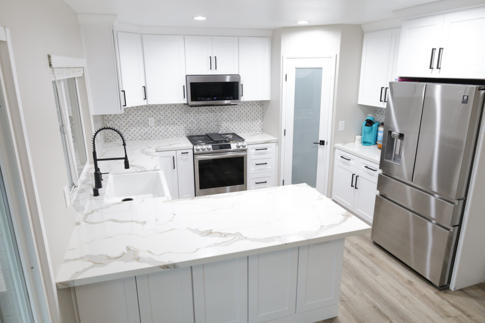 Inspiration for a mid-sized modern eat-in kitchen in San Diego with a farmhouse sink, shaker cabinets, white cabinets, quartz benchtops, white splashback, mosaic tile splashback, stainless steel appliances, laminate floors, a peninsula, grey floor and white benchtop.