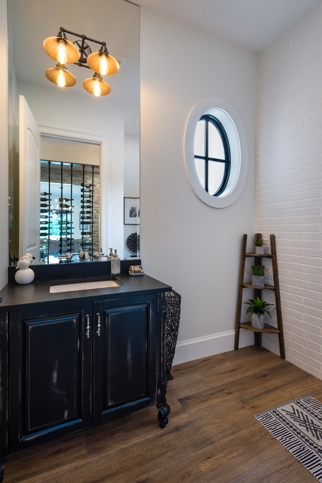 Large transitional powder room in Vancouver with raised-panel cabinets, distressed cabinets, a two-piece toilet, white tile, subway tile, white walls, medium hardwood floors, an undermount sink, engineered quartz benchtops and brown floor.