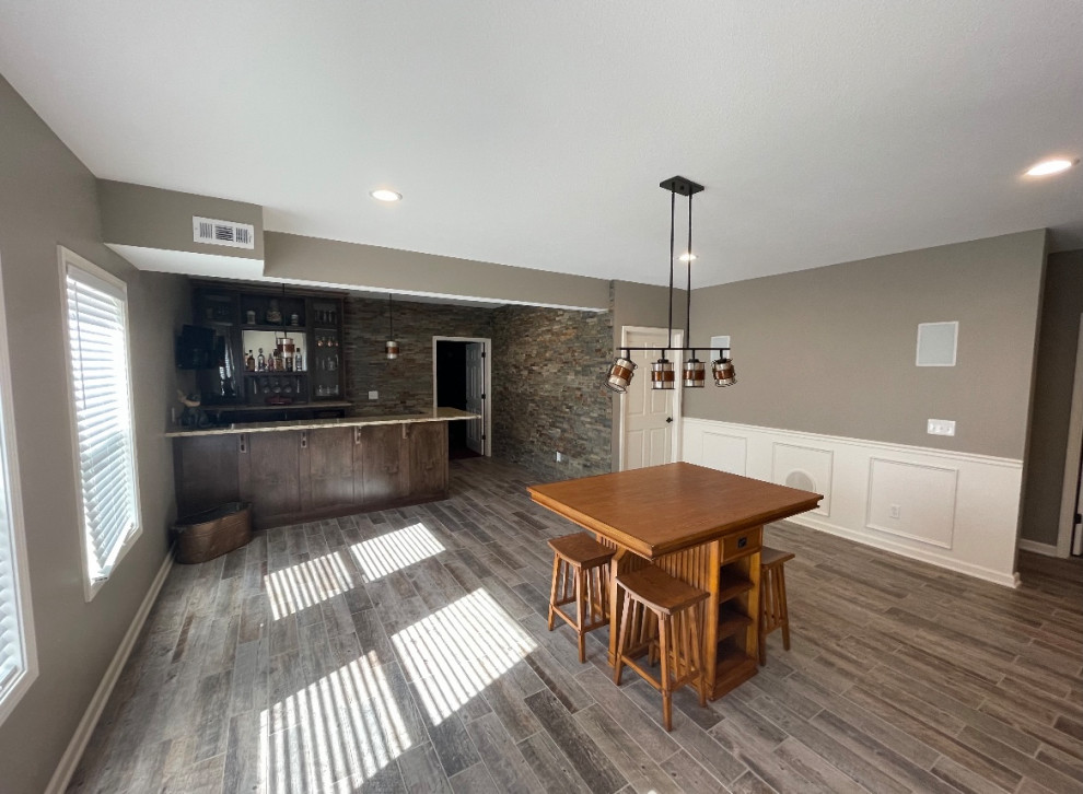 Imagen de sótano con puerta de estilo americano grande con bar en casa, paredes beige, suelo de baldosas de cerámica y suelo gris