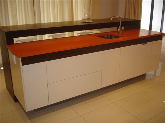 Photo of a traditional u-shaped kitchen in Other with a double-bowl sink, flat-panel cabinets, white cabinets, solid surface benchtops, brown splashback, glass sheet splashback, stainless steel appliances, light hardwood floors and with island.