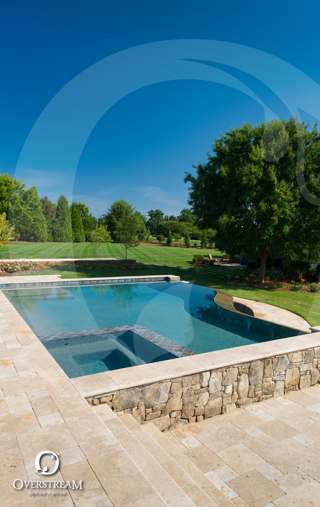 Photo of a large modern backyard custom-shaped infinity pool in Charlotte with a hot tub and natural stone pavers.