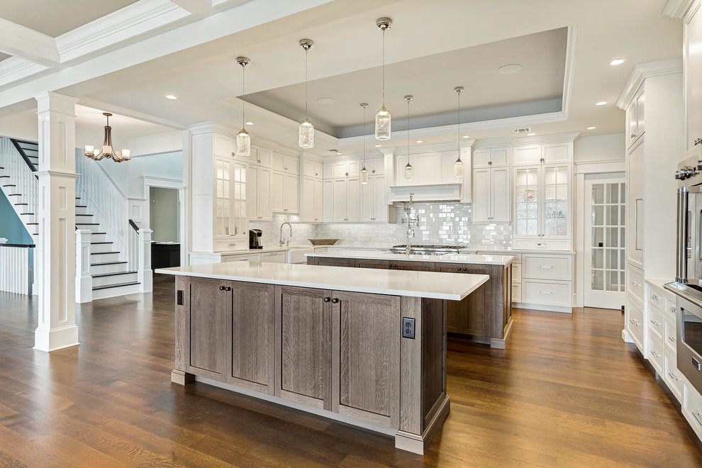 This is an example of a large transitional u-shaped eat-in kitchen in New York with a farmhouse sink, recessed-panel cabinets, white cabinets, quartz benchtops, white splashback, stone tile splashback, stainless steel appliances, medium hardwood floors and multiple islands.