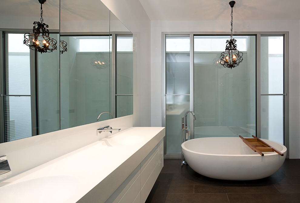 Photo of a large modern bathroom in Melbourne with an integrated sink, flat-panel cabinets, white cabinets, engineered quartz benchtops, a freestanding tub, an open shower, a wall-mount toilet, porcelain tile, porcelain floors, white tile and white walls.