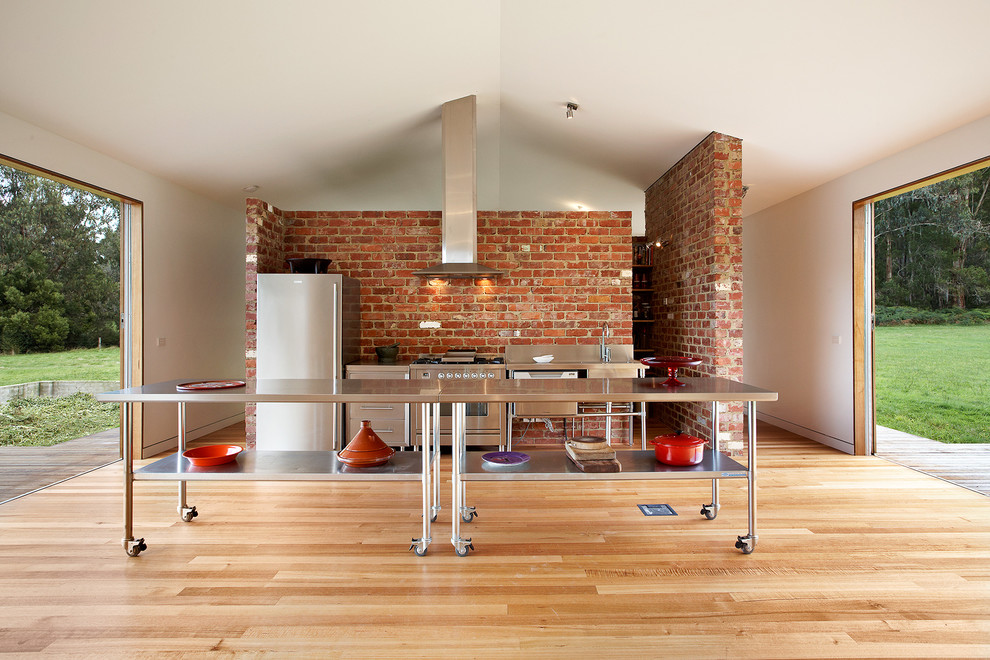 Industrial single-wall open plan kitchen in Melbourne with open cabinets, stainless steel cabinets, stainless steel benchtops, stainless steel appliances, with island and medium hardwood floors.