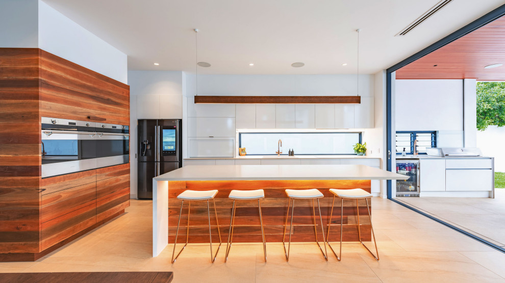 Moderne Küche in L-Form mit flächenbündigen Schrankfronten, weißen Schränken, Rückwand-Fenster, schwarzen Elektrogeräten, Kücheninsel, beigem Boden und weißer Arbeitsplatte in Brisbane