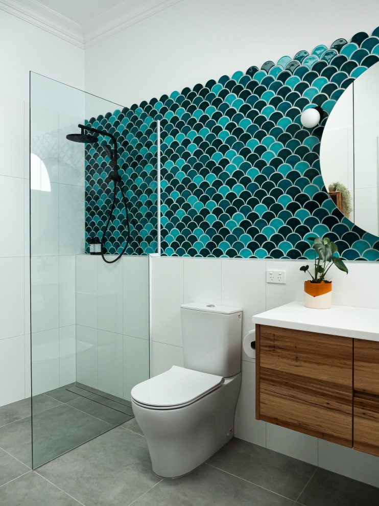 Photo of a mid-sized midcentury master bathroom in Melbourne with flat-panel cabinets, medium wood cabinets, an open shower, a wall-mount toilet, blue tile, porcelain tile, white walls, porcelain floors, an integrated sink, solid surface benchtops, grey floor, an open shower, white benchtops, a single vanity and a floating vanity.