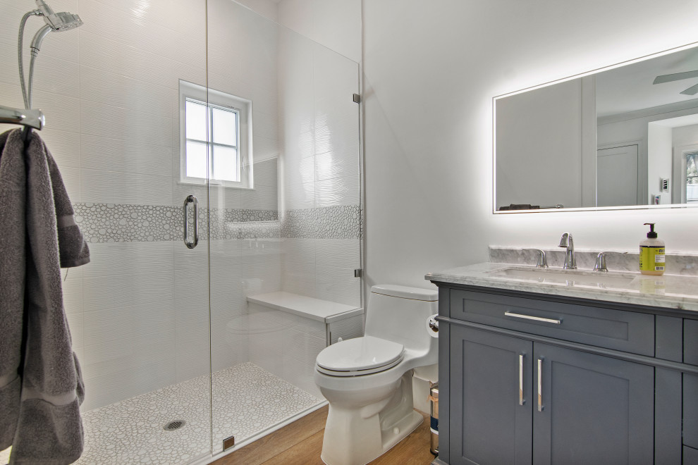Idée de décoration pour une salle de bain marine de taille moyenne avec un placard à porte shaker, des portes de placard bleues, un espace douche bain, WC à poser, un carrelage blanc, des carreaux de porcelaine, un mur blanc, un sol en vinyl, un lavabo intégré, un plan de toilette en marbre, un sol beige, une cabine de douche à porte battante, un plan de toilette gris, un banc de douche, meuble simple vasque et meuble-lavabo encastré.