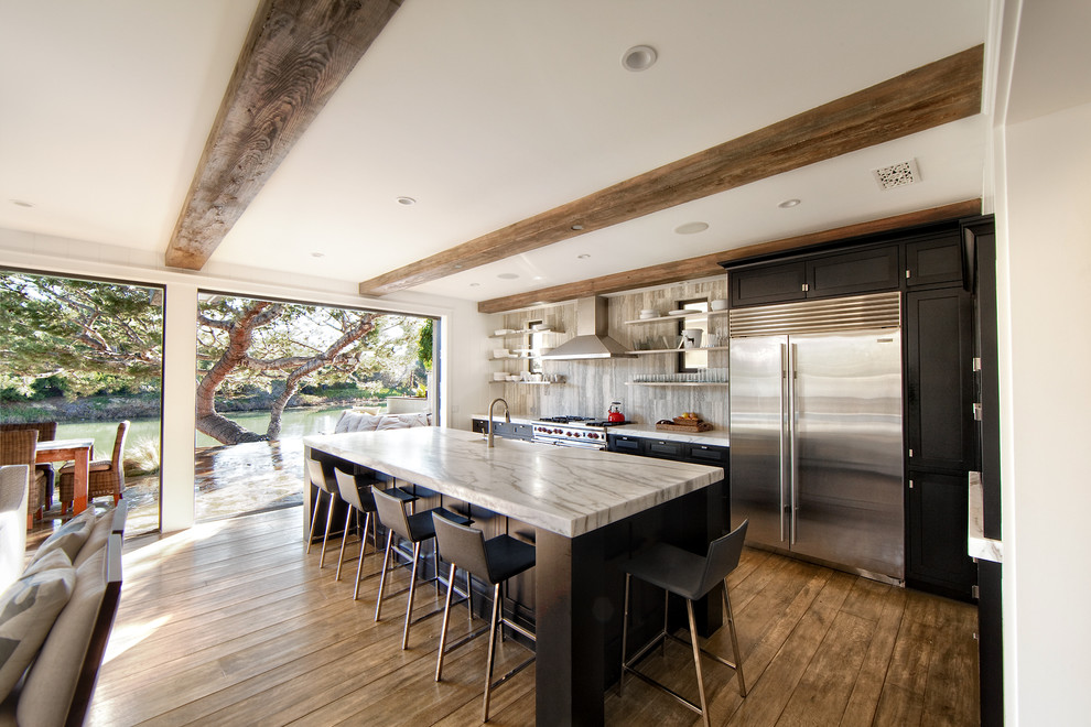 Photo of a contemporary galley open plan kitchen in Orange County with a farmhouse sink, open cabinets, black cabinets, marble benchtops, grey splashback, stone slab splashback, dark hardwood floors, with island and brown floor.